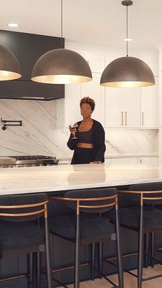 a woman standing at the bar in a kitchen with four lights hanging over her head