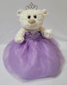 a white teddy bear wearing a purple dress with a tiara on it's head