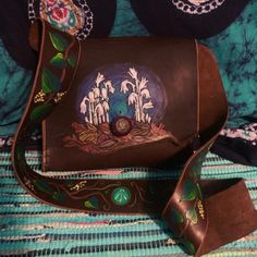 a hand painted leather purse sitting on top of a blue and green cloth covered bed