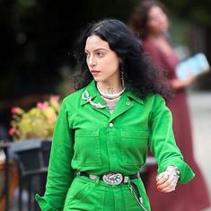 a woman in a green suit is walking down the street with her hand on her hip