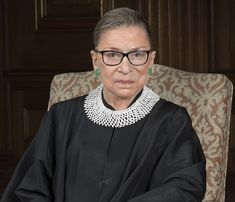 a woman sitting in a chair wearing glasses and a black dress with pearls on her neck