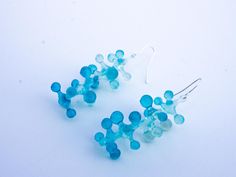 two pairs of blue glass beaded earrings on a white surface, one is dangling from the earwires