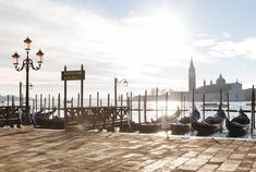 some gondolas are sitting on the water in front of a light pole and clock tower