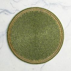 a round placemat on a marble surface with green and gold trimming around it