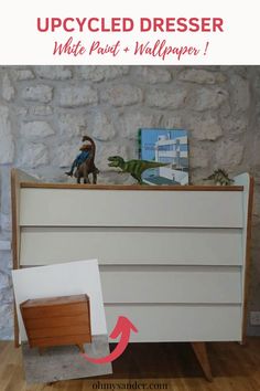 an upcycled dresser with white paint and wallpaper on the bottom, next to a toy dinosaur