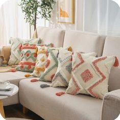 a couch with pillows on top of it in front of a potted plant and window