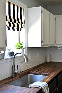 a kitchen sink sitting under a window next to a wooden counter top with a potted plant