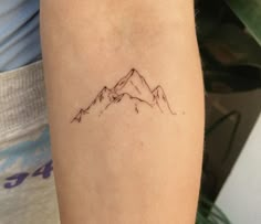 a woman's arm with a small tattoo of mountains on the back of her arm