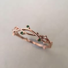 a gold ring with leaves and green stones on the side, sitting on a table