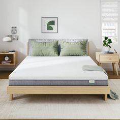 a bed with a wooden frame and green pillows in a white room next to two nightstands