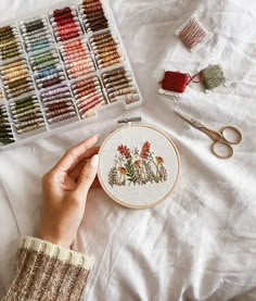 a person is holding a needle and thread in front of some embroiderying supplies on a bed