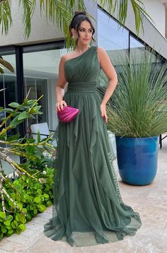 a woman in a green dress standing next to some plants and holding a pink purse