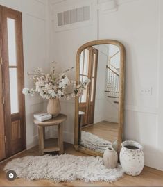 a vase with flowers on a table next to a large mirror and a small stool