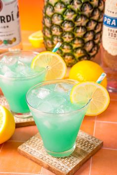 two glasses filled with blue liquid and lemons on a table next to pineapples