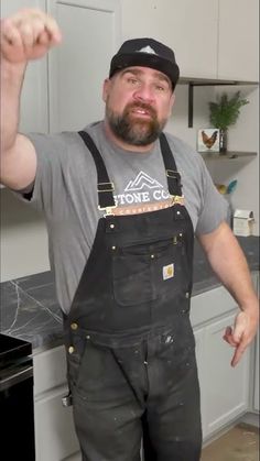 a man in overalls pointing at the camera while standing in front of a stove