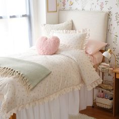 a bed with pink and green pillows on top of it next to a white headboard