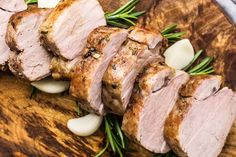 sliced pork on a wooden cutting board with onions and rosemary garnish, ready to be served