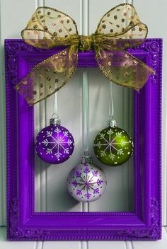 three ornaments are hanging in a purple frame with a bow on the front and side