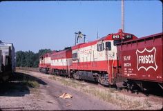 a red and white train traveling down tracks next to a dirt road with trees in the background