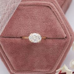 an engagement ring sits on top of a pink velvet box with white flowers in the background