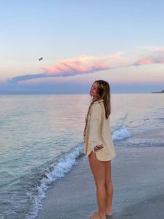 a woman is standing on the beach at sunset