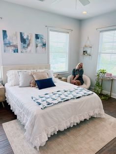 a woman sitting on the edge of a bed in a room with white walls and wooden floors