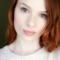 a woman with red hair and blue eyes is looking at the camera while wearing a white sweater