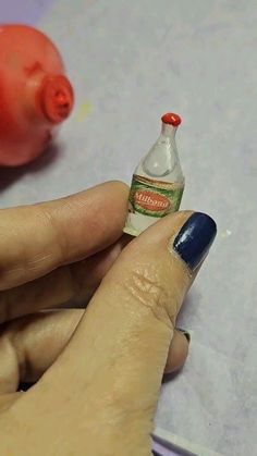 a person holding a miniature bottle in their hand next to an eraser on a piece of paper