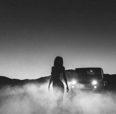 a woman standing in front of a truck on a foggy road with the lights on