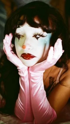 a woman with her hands on her face and eyes painted white, posing for the camera