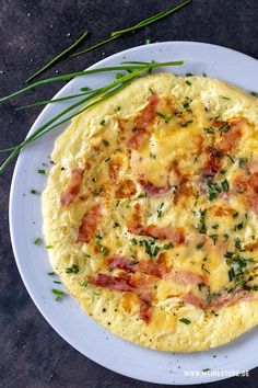 a white plate topped with an omelet covered in cheese and bacon next to green onions