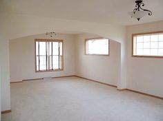 an empty room with two windows and a chandelier hanging from the ceiling,