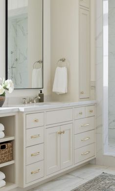 a bathroom with white cabinets and marble counter tops, along with a large mirror on the wall