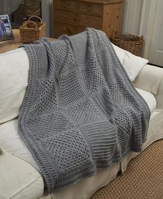 a large gray knitted blanket sitting on top of a white couch