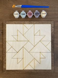 a wooden puzzle with four different shapes on it and paintbrushes next to it