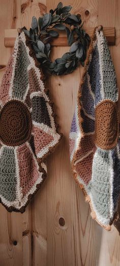 two crocheted hats are hanging on a wooden wall next to a green wreath