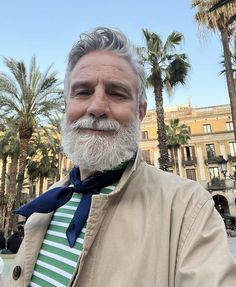 an older man with grey hair and beard wearing a striped tie in front of palm trees