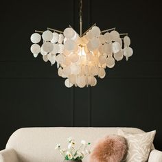 a chandelier hanging over a couch with pillows and flowers on the table next to it