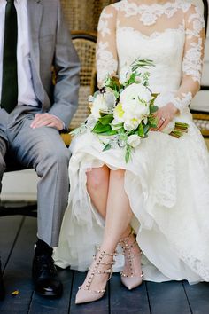 a bride and groom sitting on a bench in front of a wicker chair with white flowers