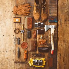 an assortment of men's accessories laid out on a wooden table, including shoes, gloves and other items