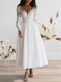 a woman in a white dress standing on a wooden floor next to flowers and branches