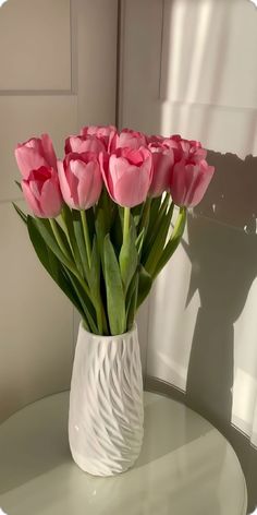 a white vase filled with pink flowers on top of a table