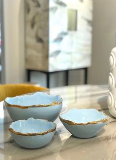 three blue bowls sitting on top of a counter next to a white vase with gold trim