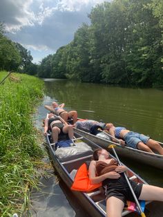 several people in canoes paddling down a river with tall grass and trees behind them