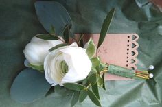 a boutonniere with white flowers and greenery on a green cloth background