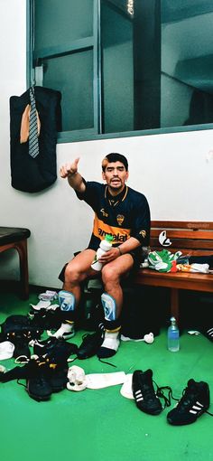 a man is sitting on a bench surrounded by shoes and other sports equipment, with his hand up in the air