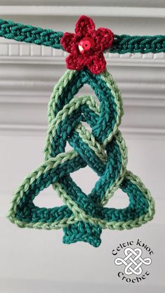 a crocheted christmas tree ornament hanging from a string with a red flower on top