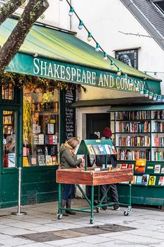 two people standing in front of a book store with bookshelves on the sidewalk