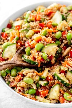 a white bowl filled with vegetables and rice next to a wooden spoon on top of a table