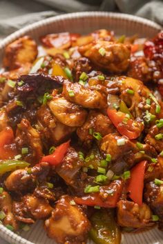 a white bowl filled with chicken and vegetables on top of a wooden table next to a fork